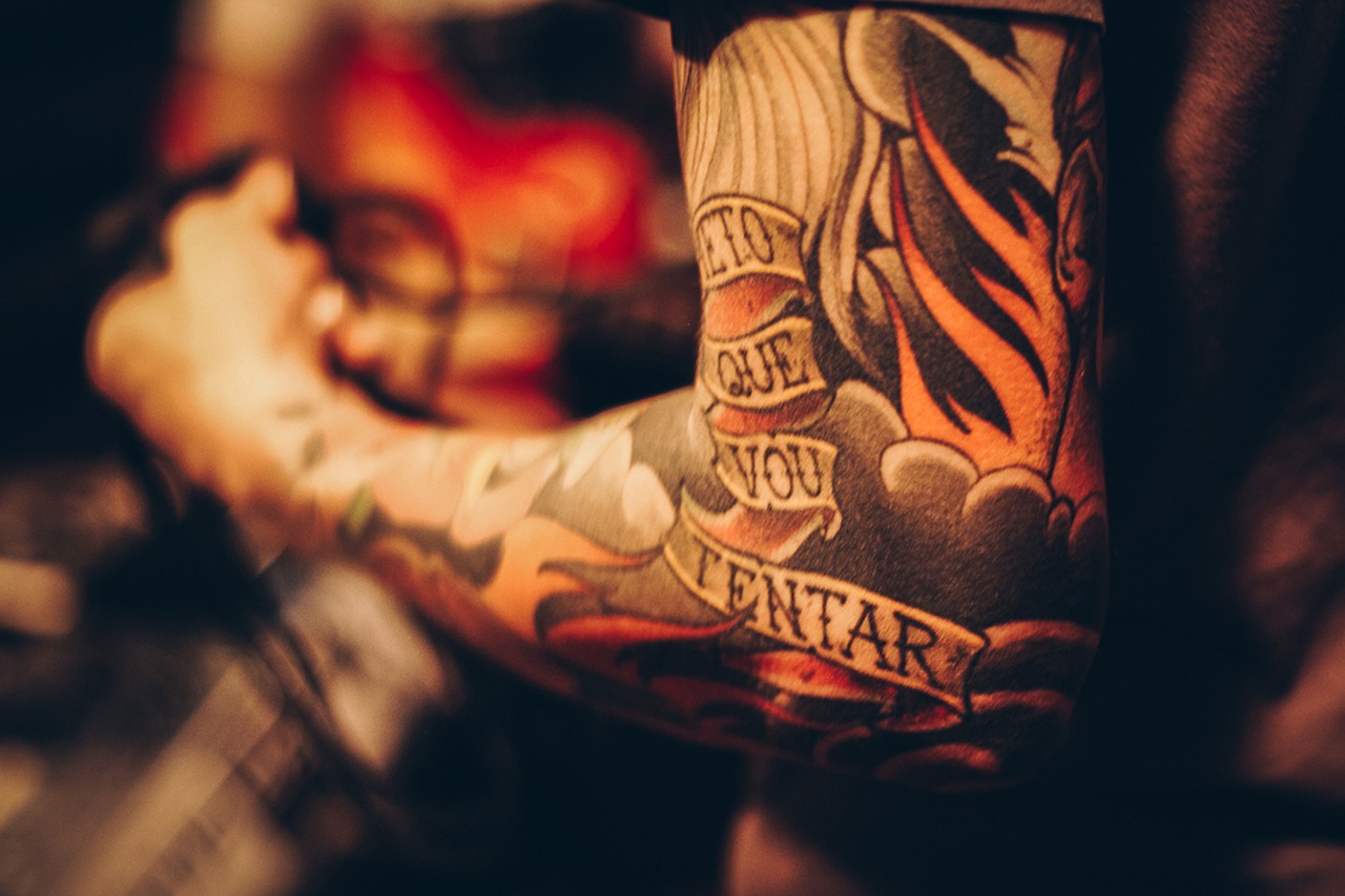 Imagen de un brazo con un tatuaje en negro y llamas. Lleva un mensaje en el tatuaje y parece que tenga el brazo en un apoyabrazos de un estudio