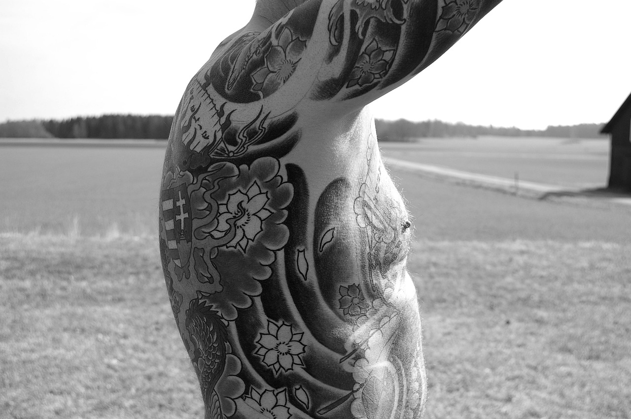 Se ve un hombre en medio del campo. Tiene las costillas y el pecho tatuados y los brazos en alto